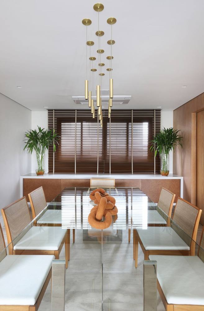 Sala de jantar com pendentes dourados e mesa de vidro